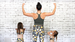 Pureform Pilates founder and owner Lindsay Davis-Hannibal with her two little girls in matching activewear facing the studio wall with their arms up showing strength.