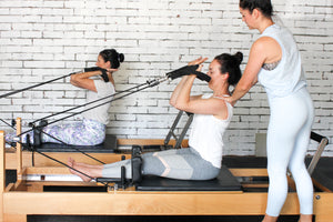 Pureform Pilates founder and owner Lindsay Davis-Hannibal teaching two clients in the studio, who are doing a reformer class.